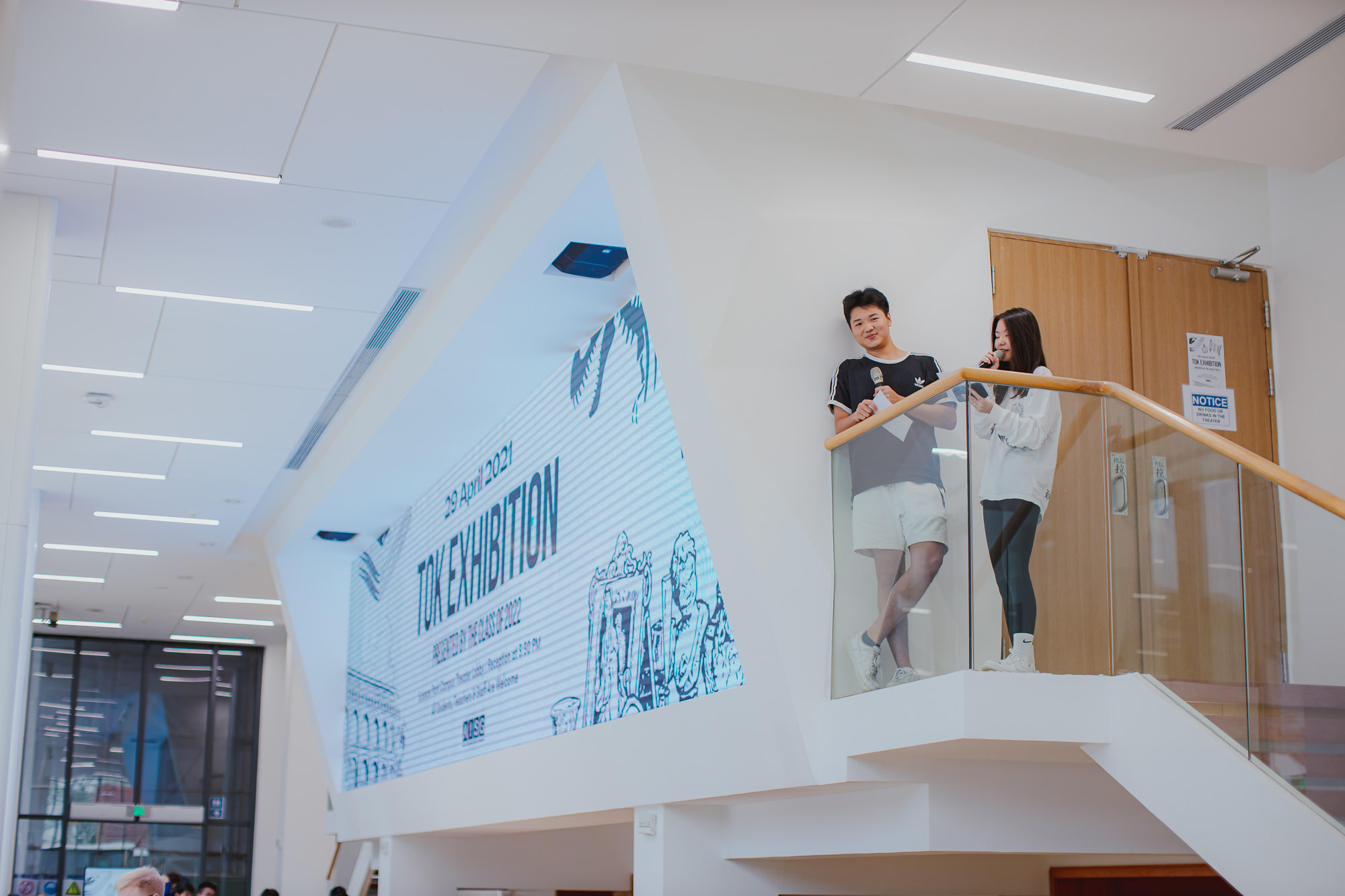 two students standing at the top of the stairs talking into microphones