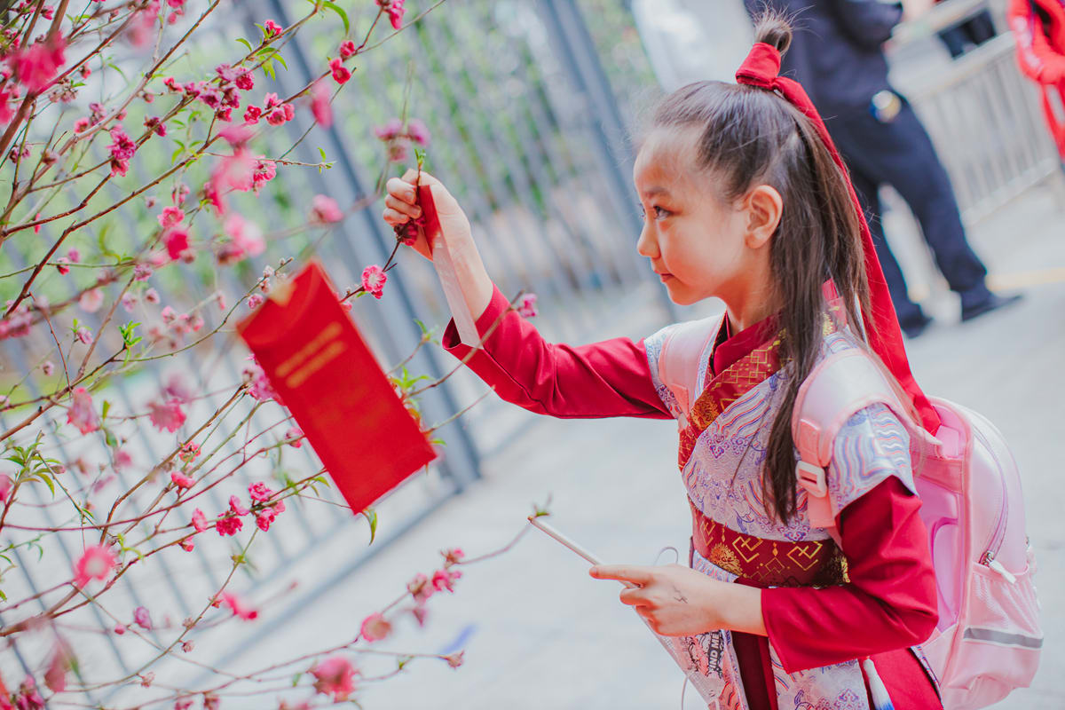 a girl hangs a giving envelope on the peach blossom tree