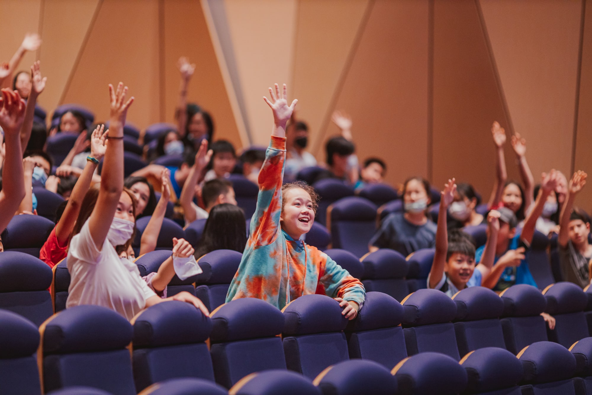students in their seats excitedly raising their hands