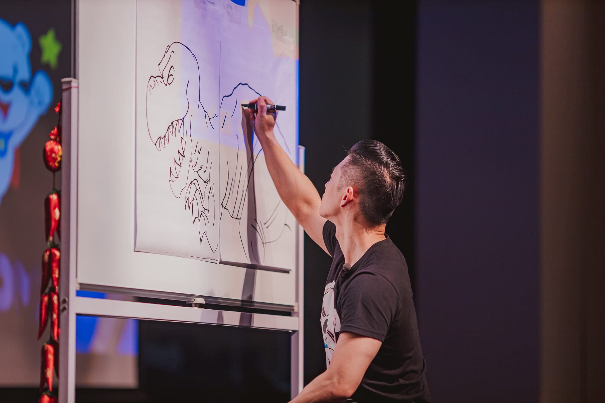 man kneeling drawing dinosaur on big pad of paper