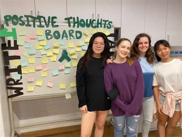 4 girls smile and pose in front of a positive thoughts board