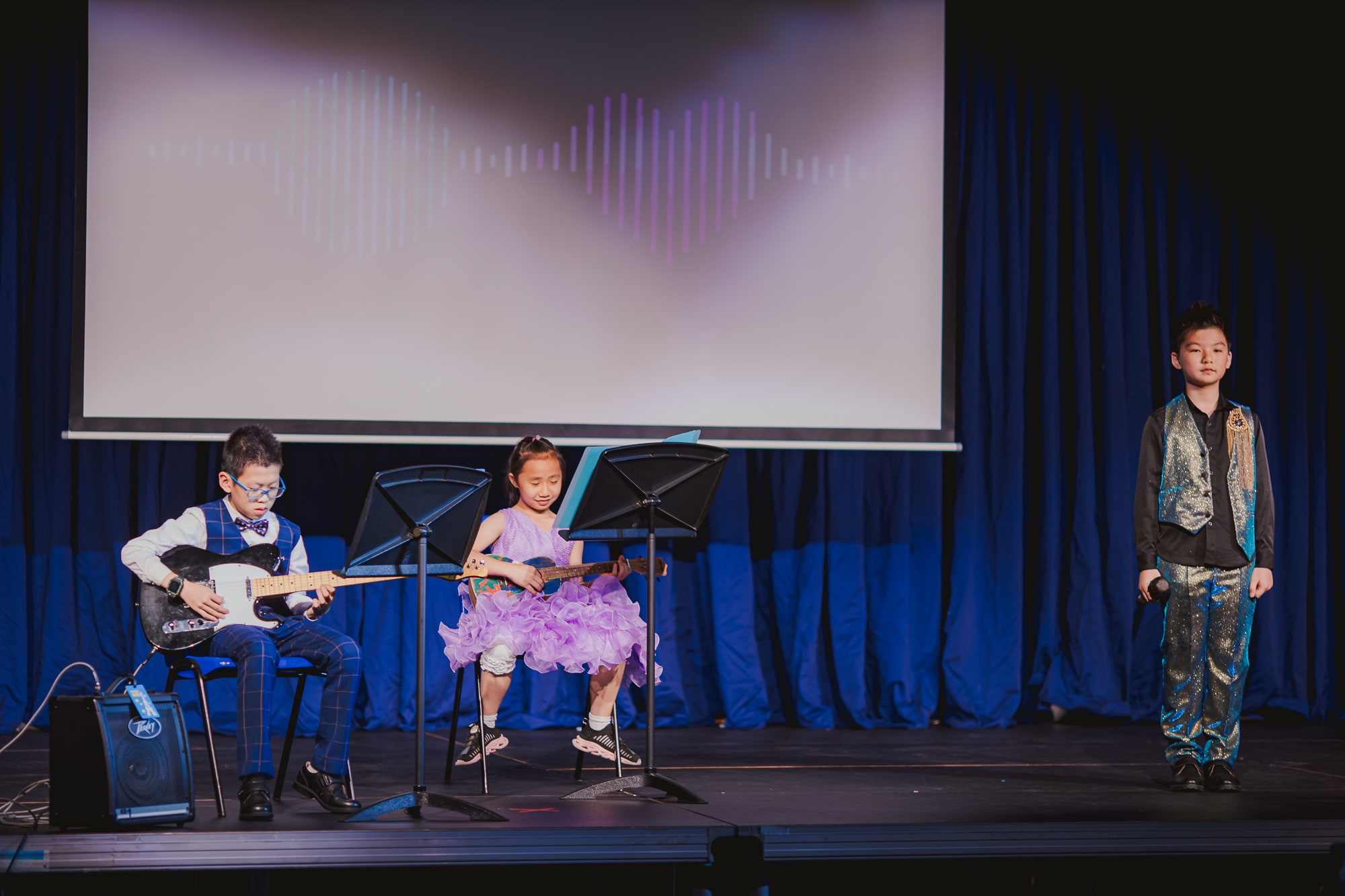 a girl and boy play guitar while a boy sings onstage