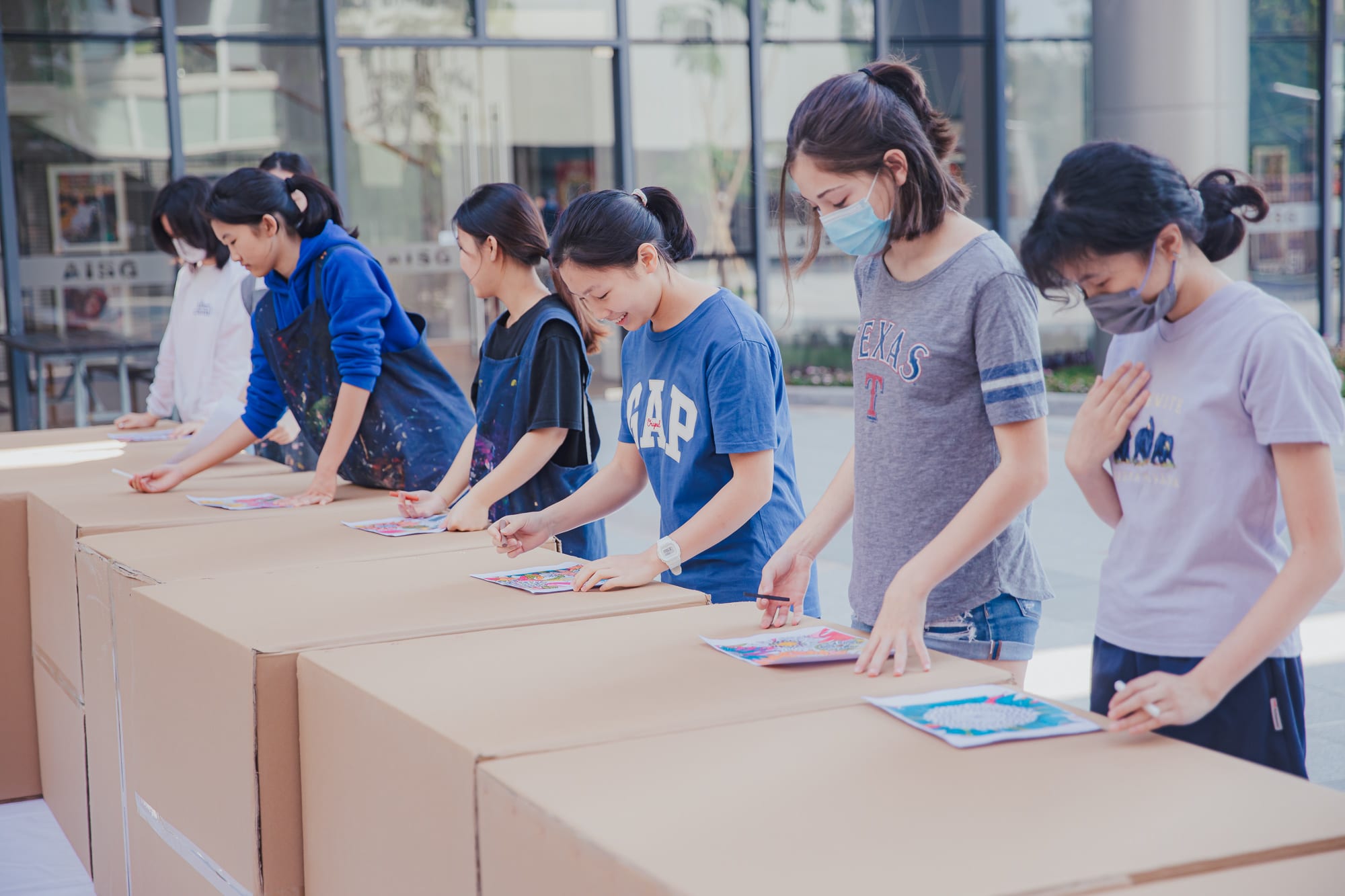 students drawing on cardboard boxes in a row