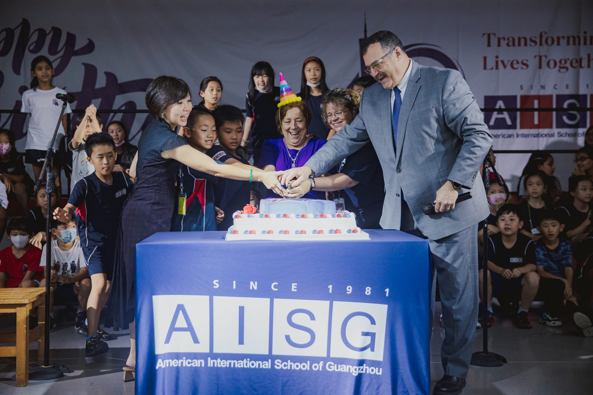 At AISG's 40th birthday celebration, cake cutting with director, elementary principal, teacher, students and parent