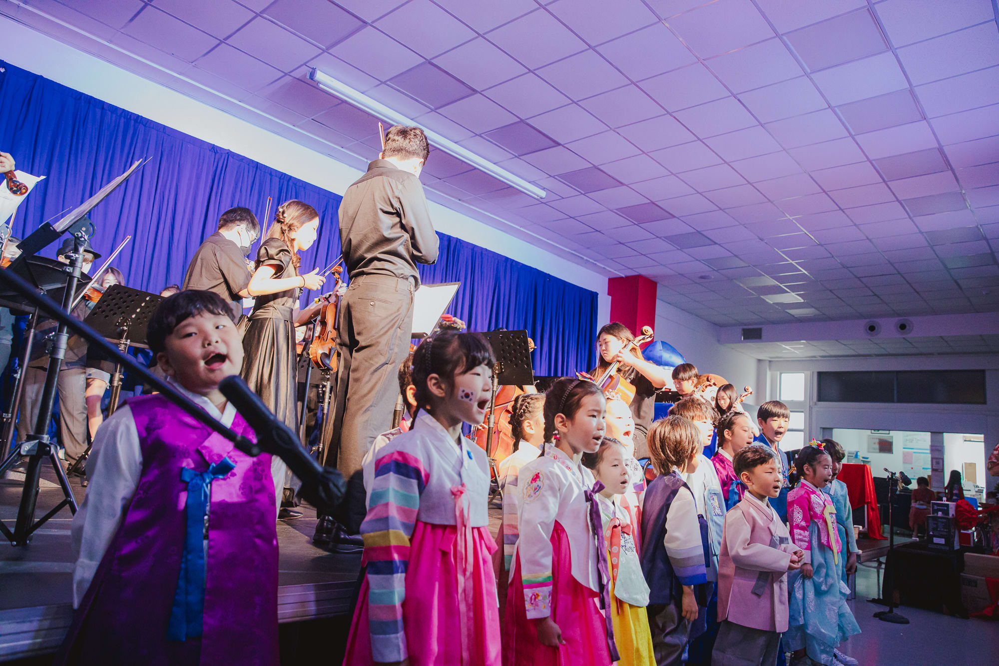 children dressed up in traditional korean outfits singing as older children play instruments onstage