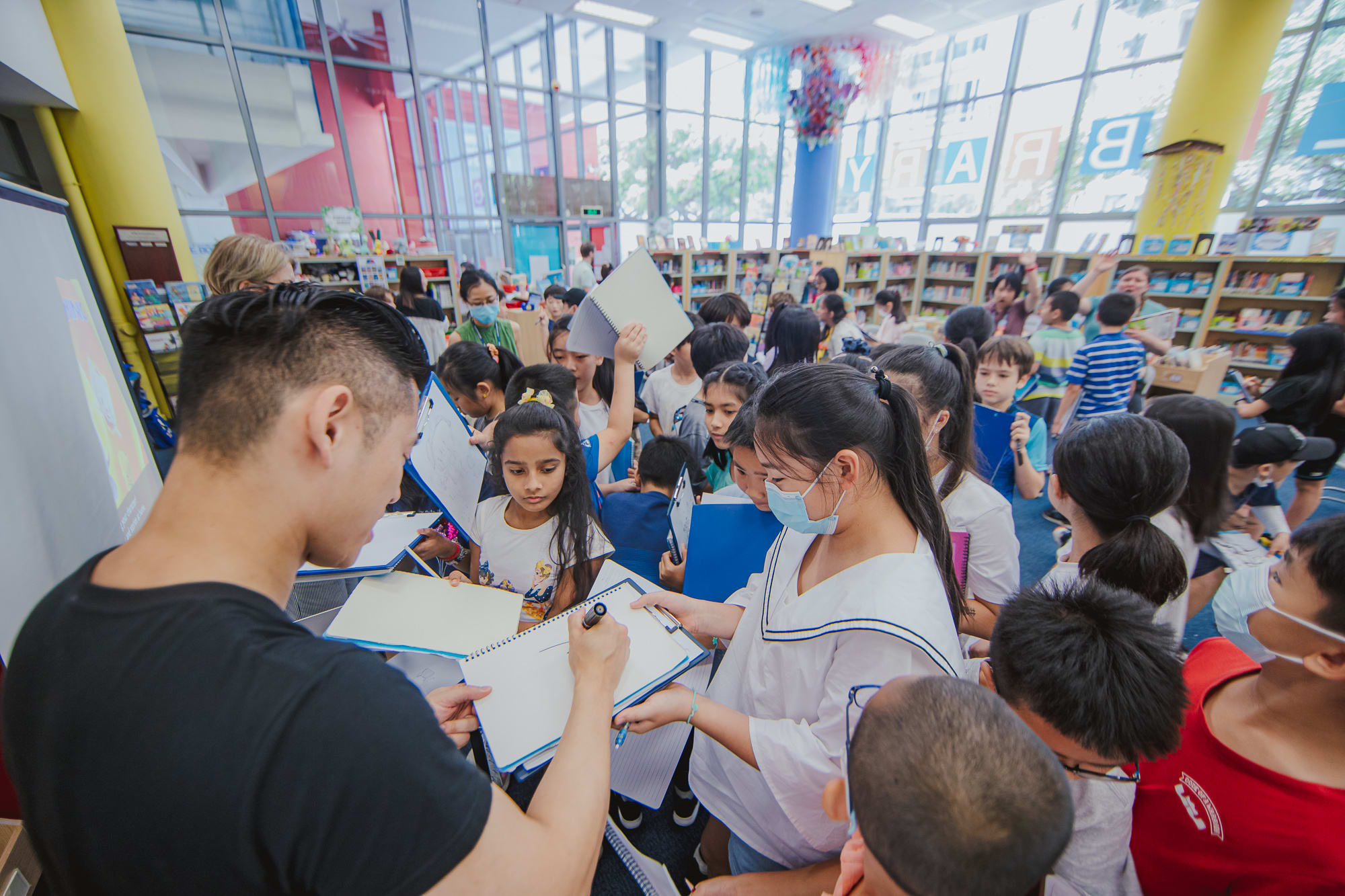 man signing pads of paper as students crowd around him
