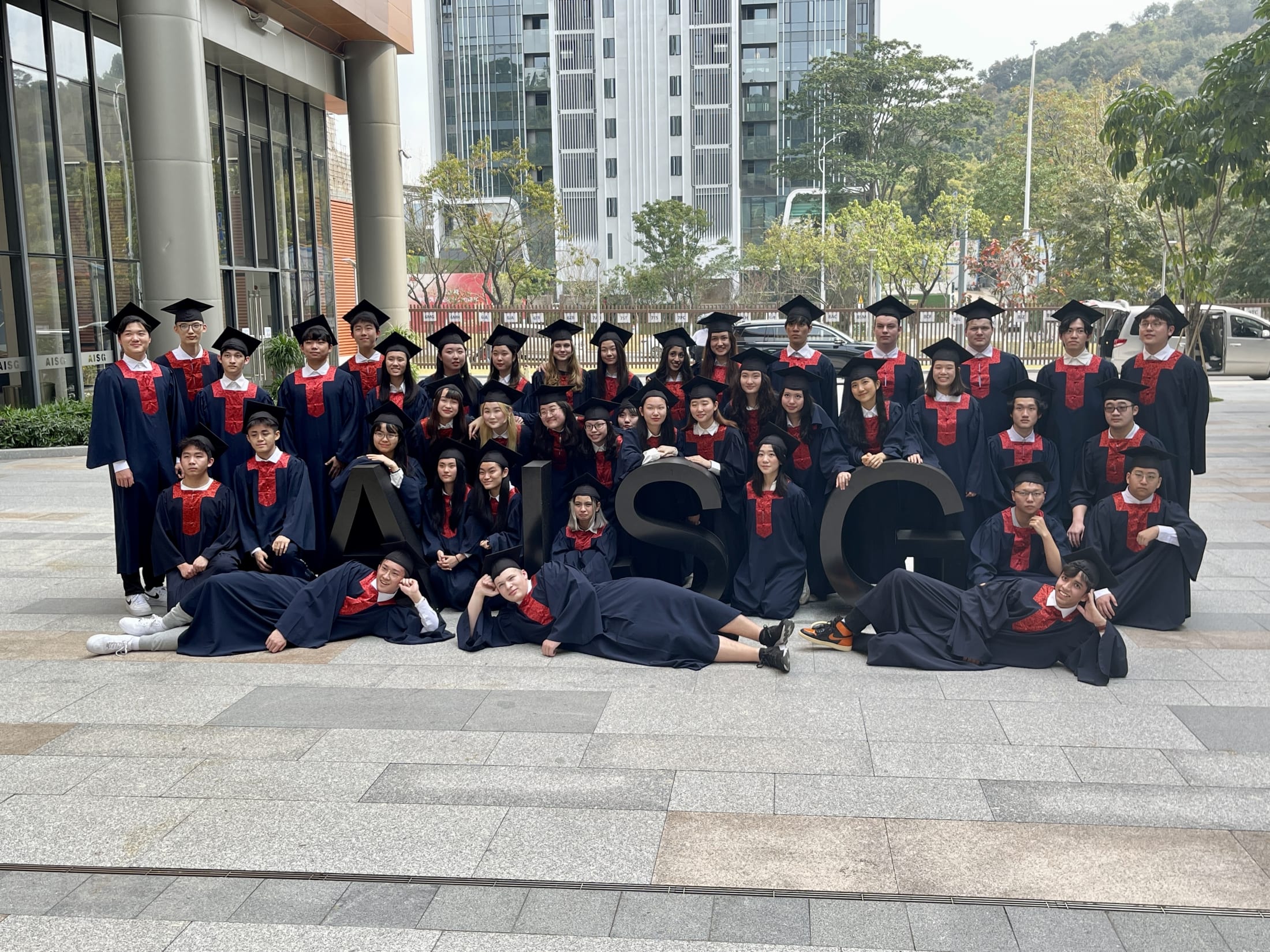 AISG Seniors with their cap and gowns standing by the AISG letters