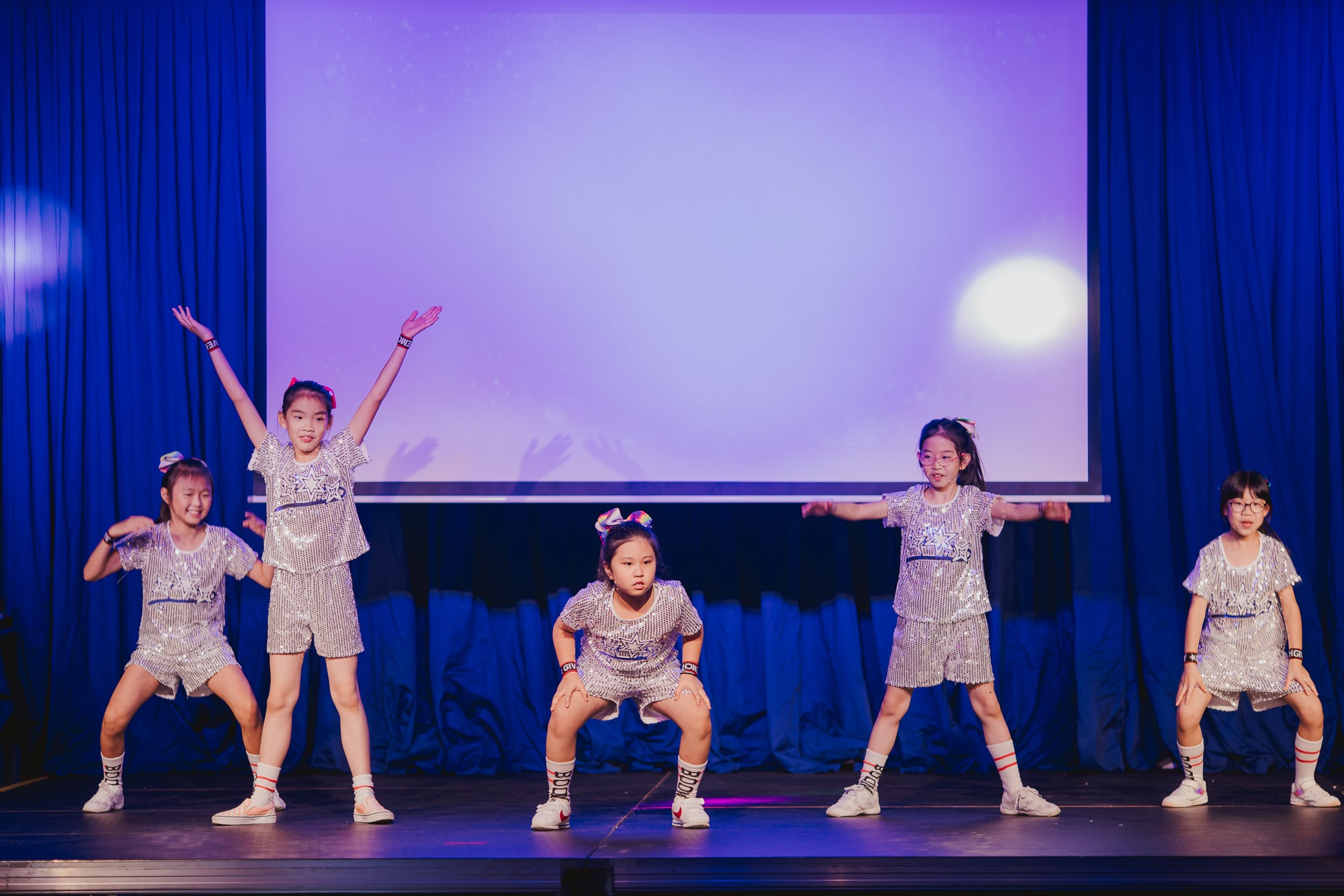 girls in sequined silver outfits doing a dance onstage